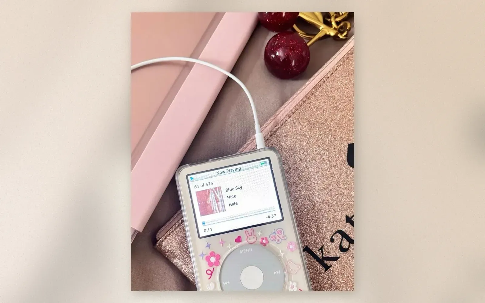 White refurbished iPod Classic in a clear case with kawaii bunny and flower stickers, Now Playing screen showing a track