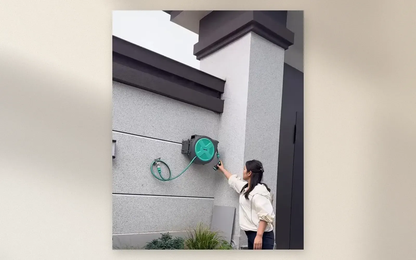 Retractable garden hose reel mounted on exterior wall with green hose