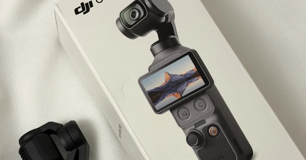 DJI Osmo Pocket 4 Gimbal-Kamera neben ihrer weissen Standard-Combo-Schachtel auf weissem Stoff