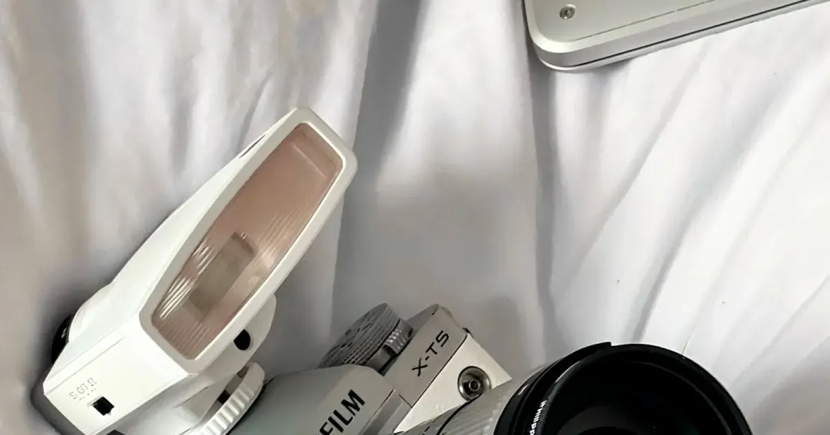 Fujifilm X-T5 silberne Systemkamera mit Sigma 18-50mm f/2.8 Objektiv, weißem Blitz und Jeans Half Case auf weißer Bettwäsche