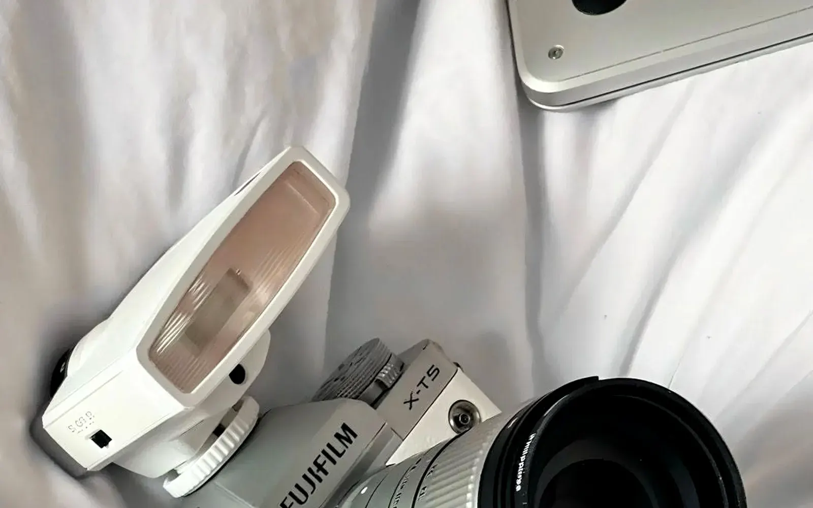 Fujifilm X-T5 silver mirrorless camera with Sigma 18-50mm f/2.8 lens, white flash and denim half case lying on white bedding