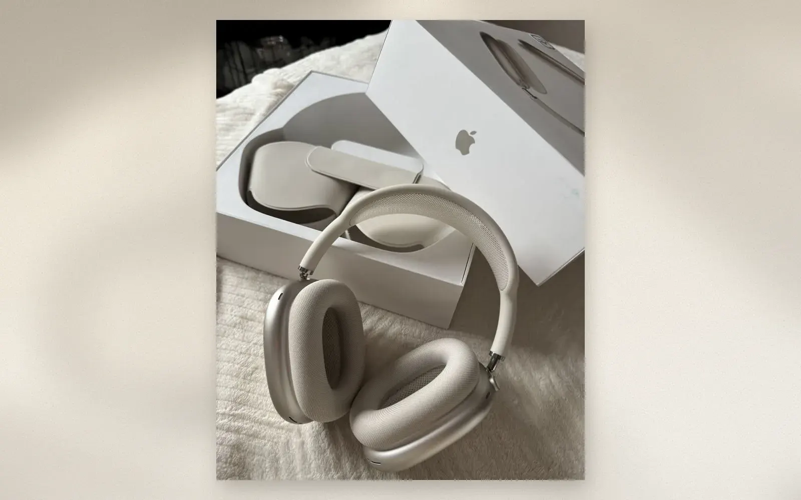 Apple AirPods Max headphones in Starlight resting on a soft blanket next to the open retail box