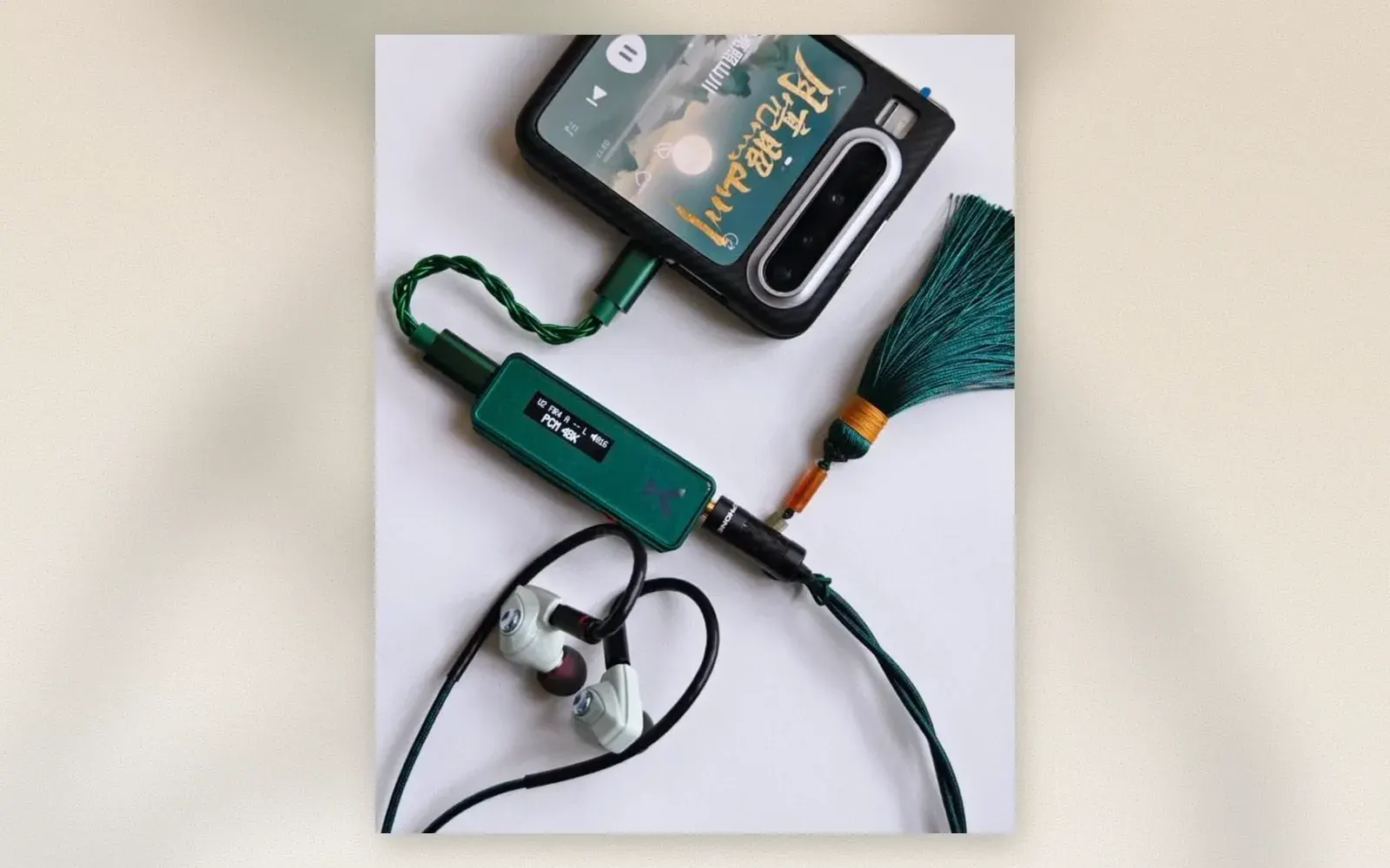 Green USB-C DAC dongle with display connected to phone and white IEMs through 4.4mm balanced cable with bead charm