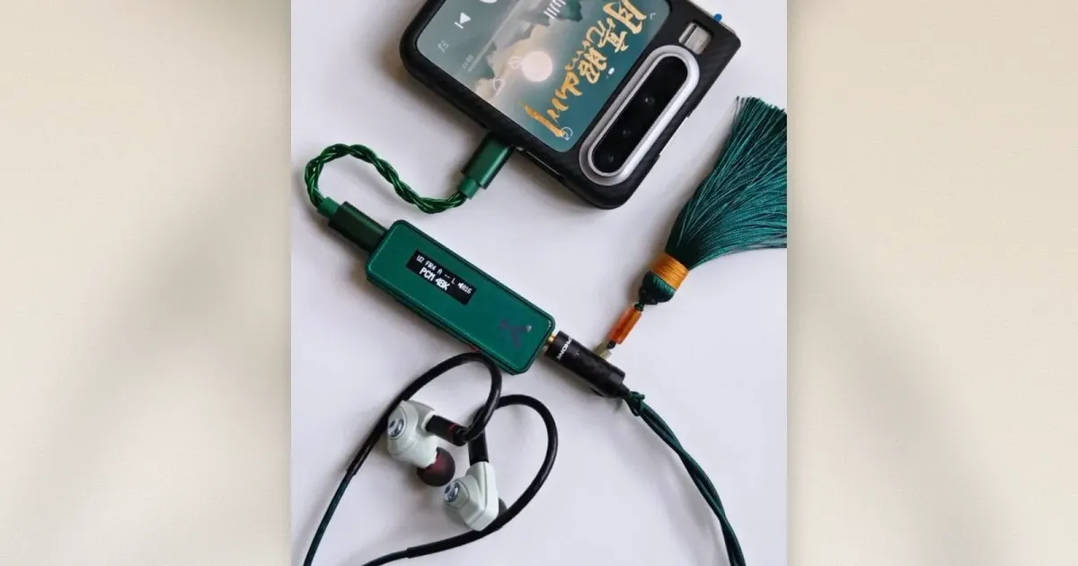 Grüner USB-C DAC-Dongle mit Display verbunden mit Phone und weißen IEMs über 4.4mm Balanced-Kabel mit Perlen-Anhänger