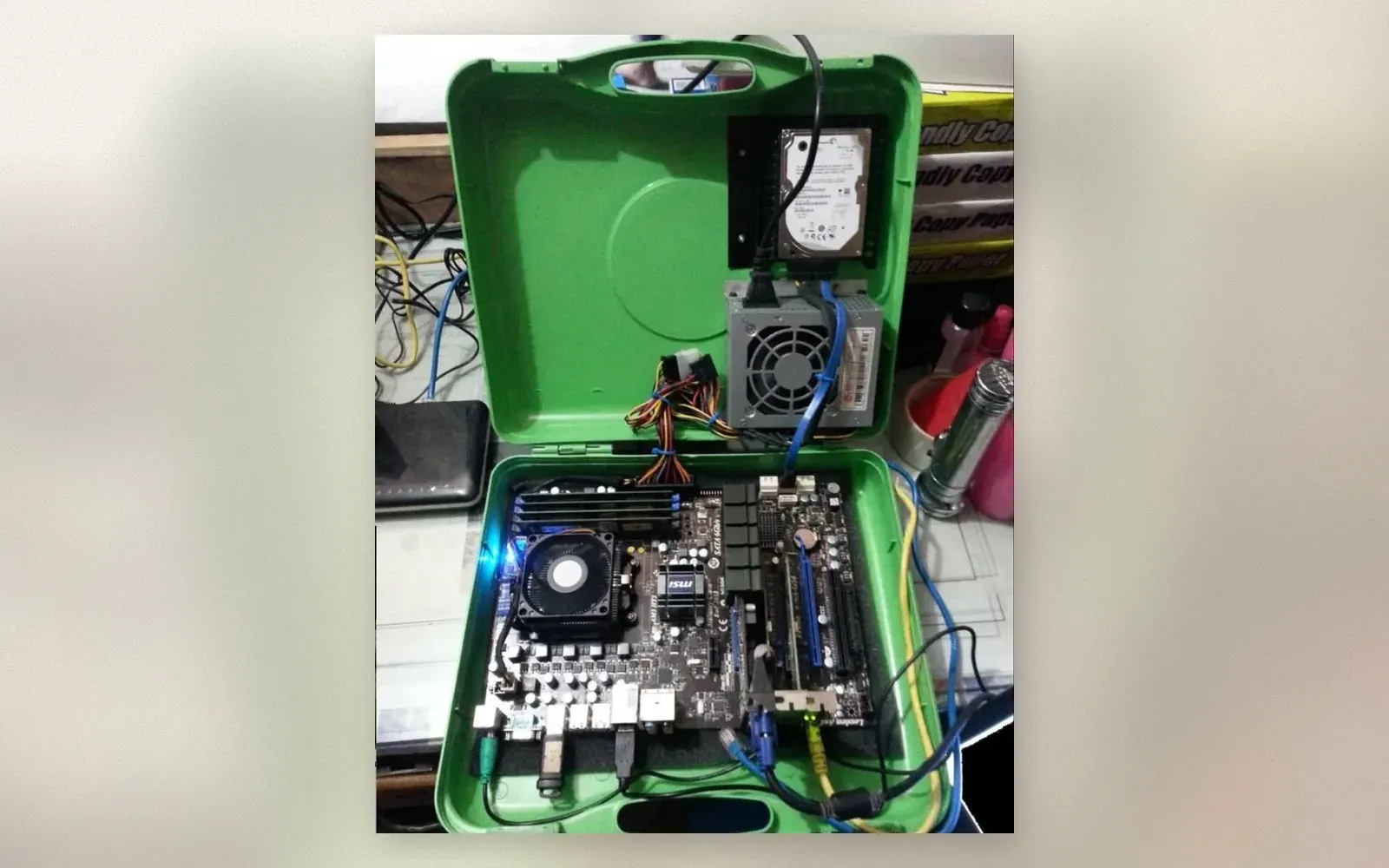 Green toolbox case opened to show MSI motherboard, CPU cooler, RAM, PSU, and hard drive mounted inside