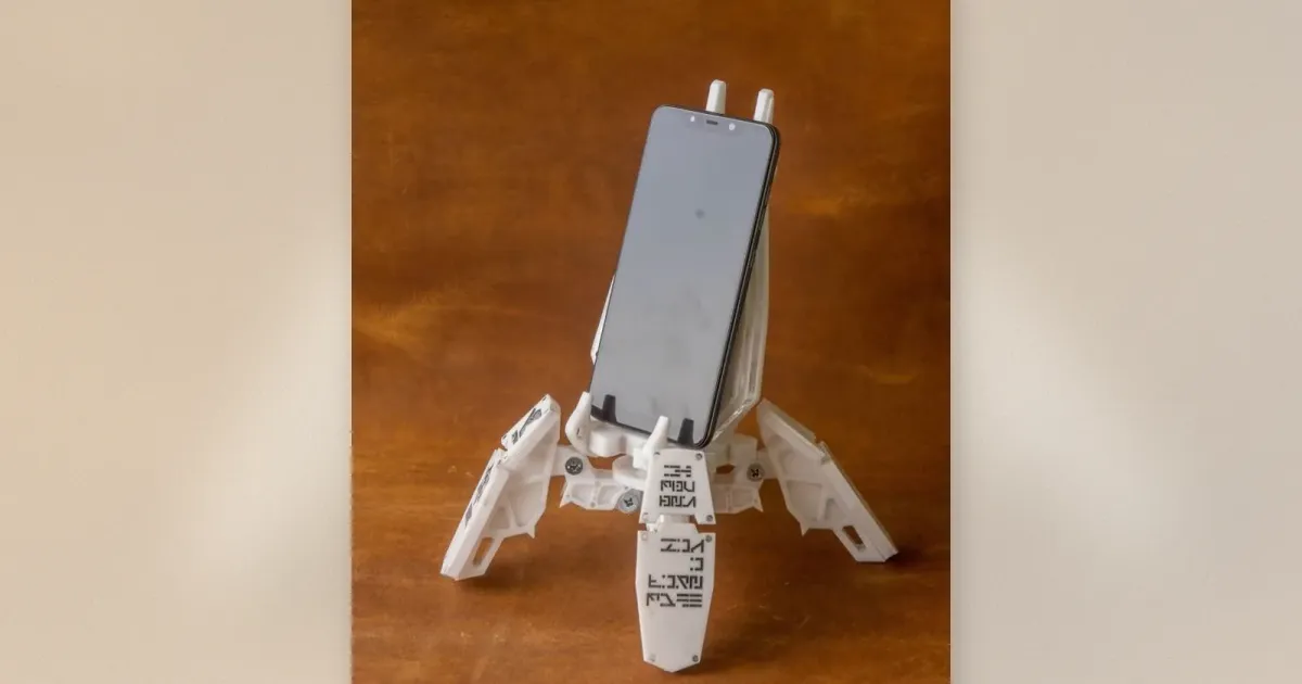 Weißer 3D-gedruckter Mech-Exo-Suit-Handyhalterung mit beweglichen Beinen, die ein Smartphone auf einem Holztisch greifen