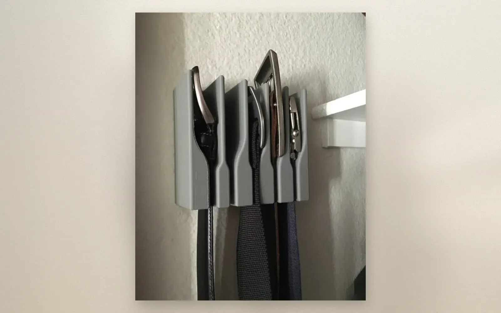Wall-mount belt hanger organizer with 5 belts hanging from grey bracket on white wall