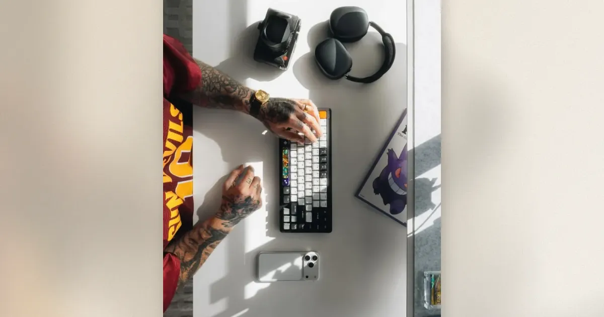 Aufsicht auf weißen Schreibtisch mit Custom-Mechanical-Keyboard, Over-Ear-Kopfhörer, Kompaktkamera und iPhone