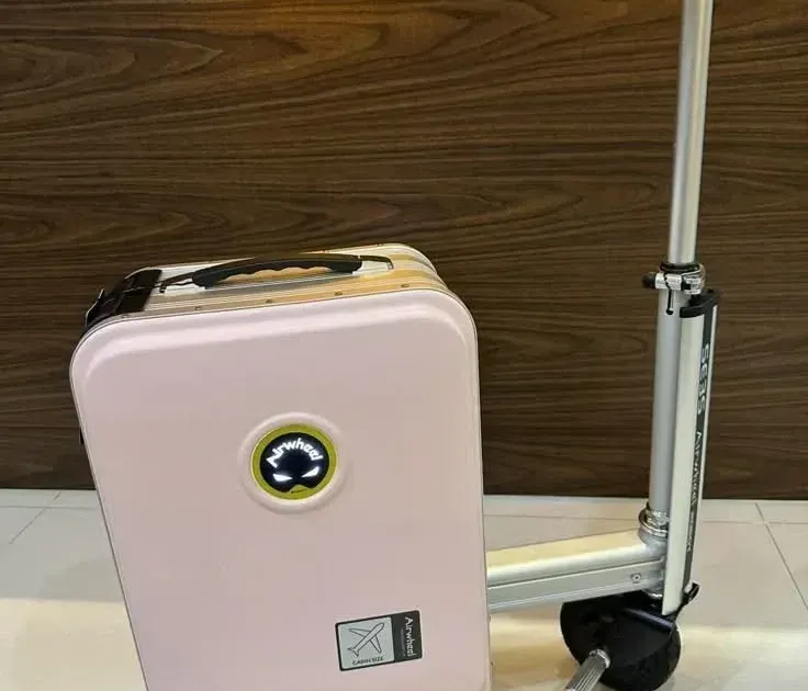 Rosa Airwheel SE3S fahrbarer Koffer mit Teleskop-Lenker und schwarzem Sattelsitz, angelehnt an eine Holzwand