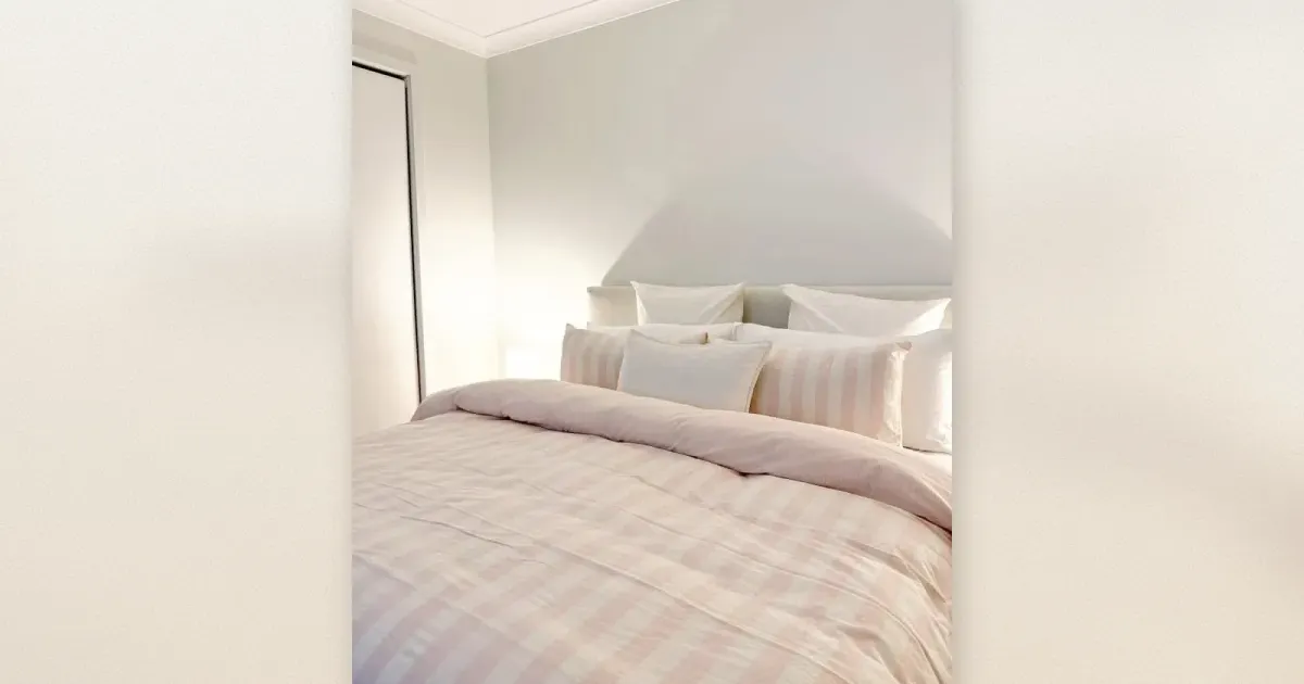 Ein Bett mit rosa weiß karierter Bettwäsche und gestreiften Kissenbezügen