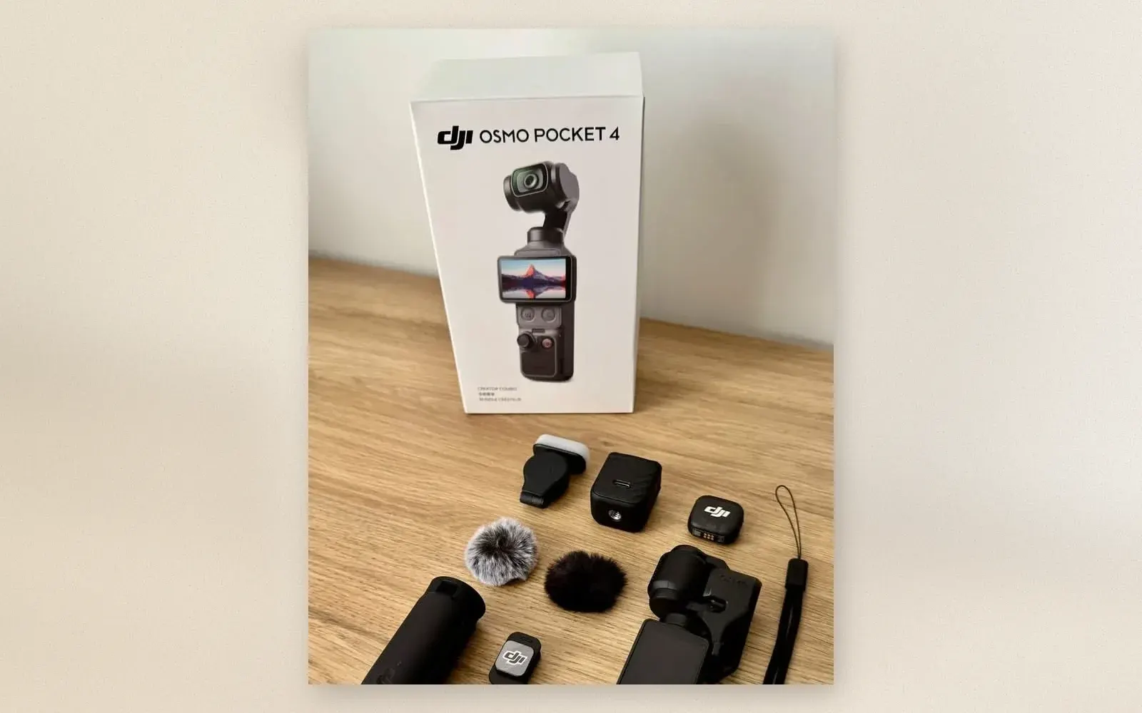 DJI Osmo Pocket 4 Creator Combo box behind the camera, mic transmitter, fill light, windscreens and accessories laid out on a wooden table