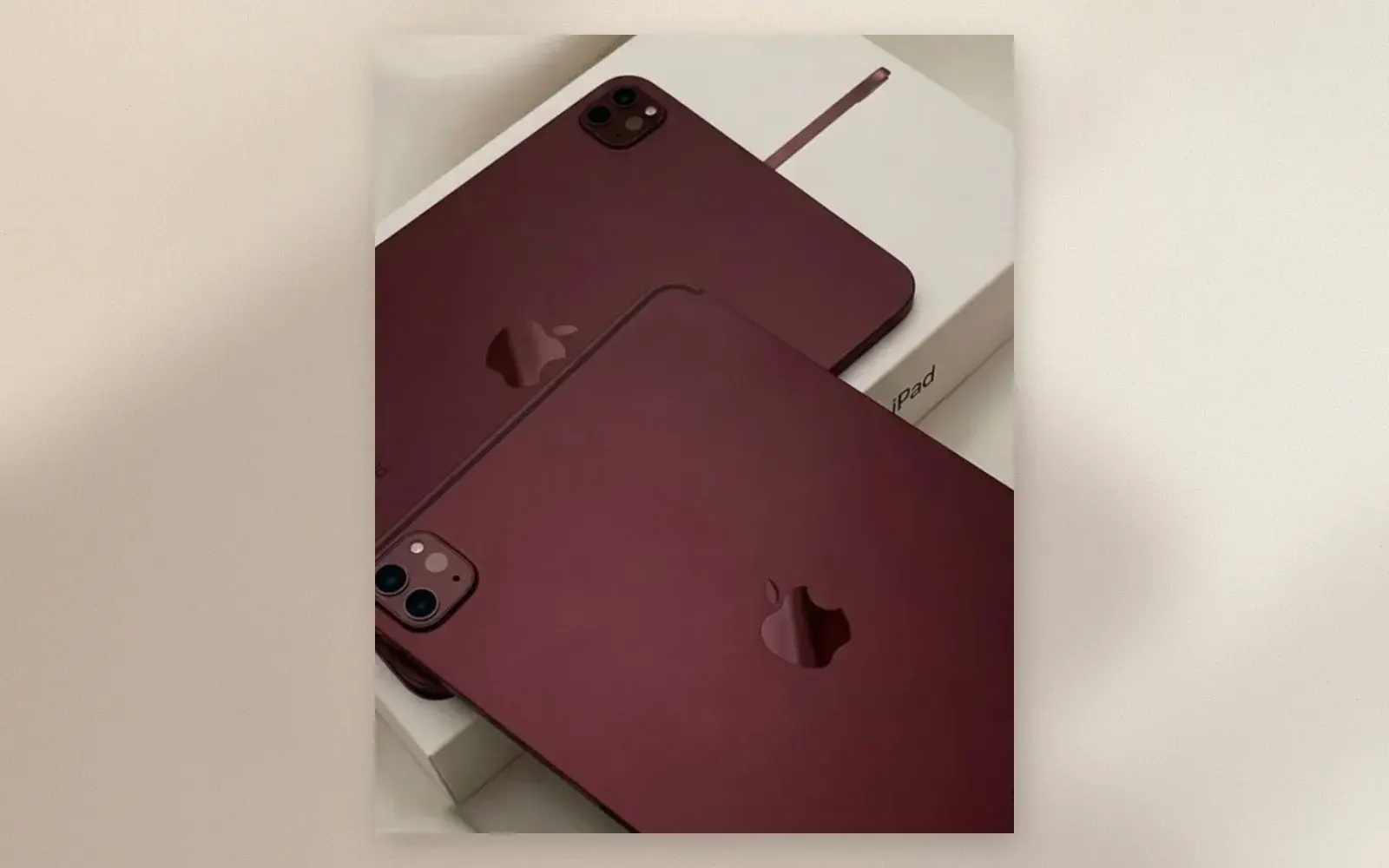 Two iPad Pros wrapped in dark burgundy vinyl skins resting on an iPad box and cream fabric