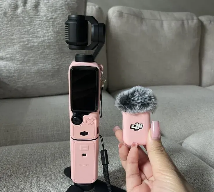 DJI Osmo Pocket 3 in a pink silicone case on its mini tripod next to a pink DJI Mic Mini transmitter with a furry wind muff