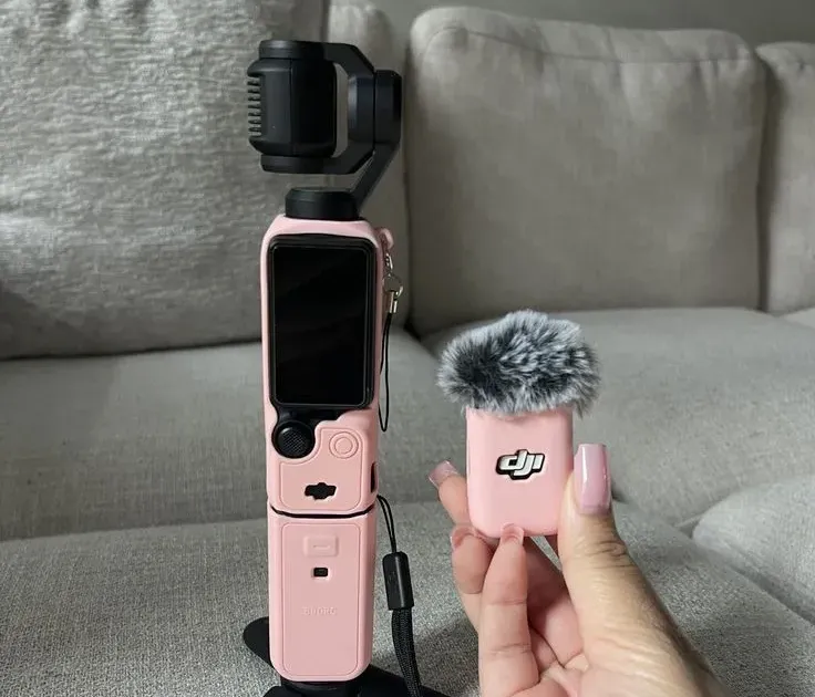 DJI Osmo Pocket 3 in pinkfarbener Schutzhülle auf dem Mini-Stativ neben einem pinkfarbenen DJI Mic Mini Sender mit Windshield