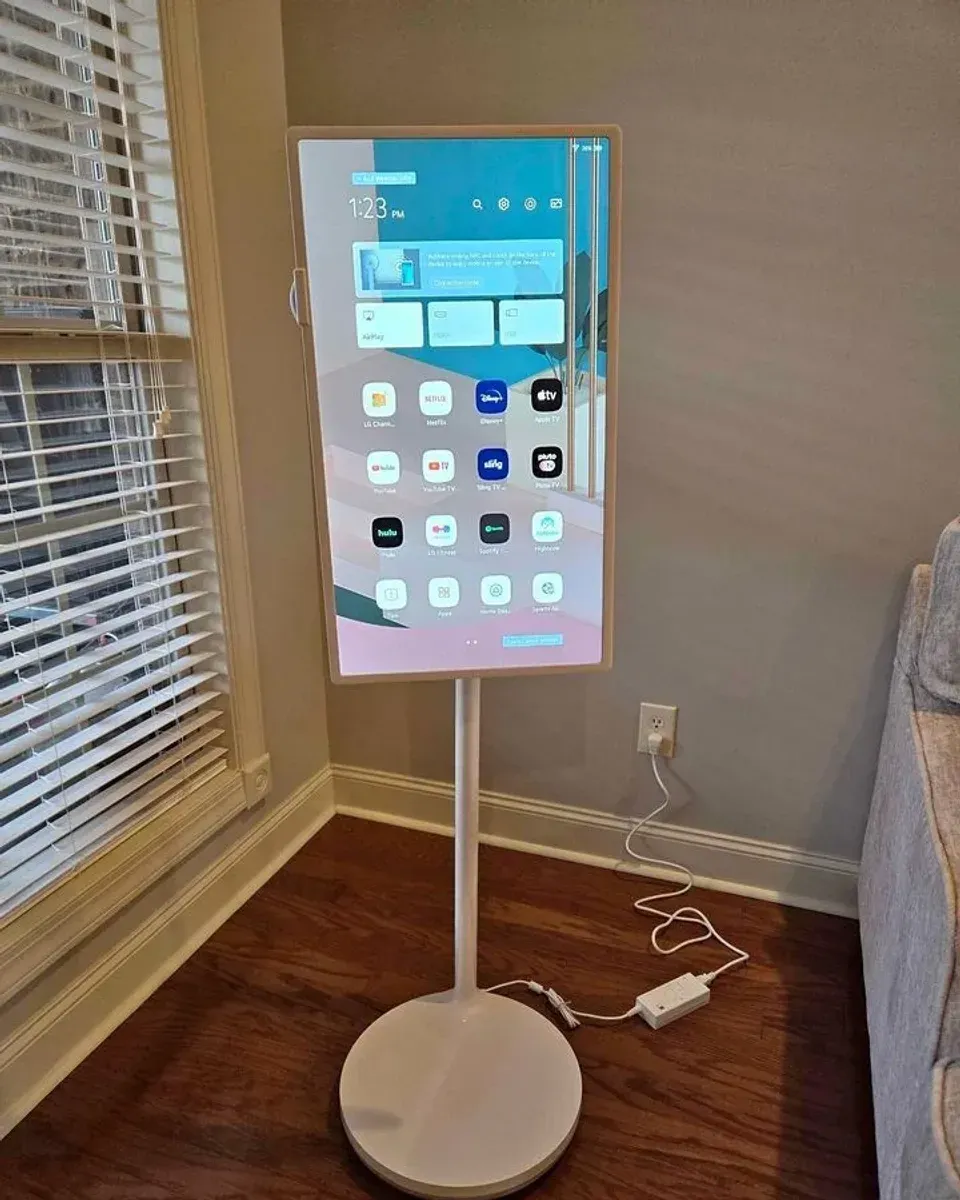 Portrait mode smart screen on a slim white floor stand beside a sofa