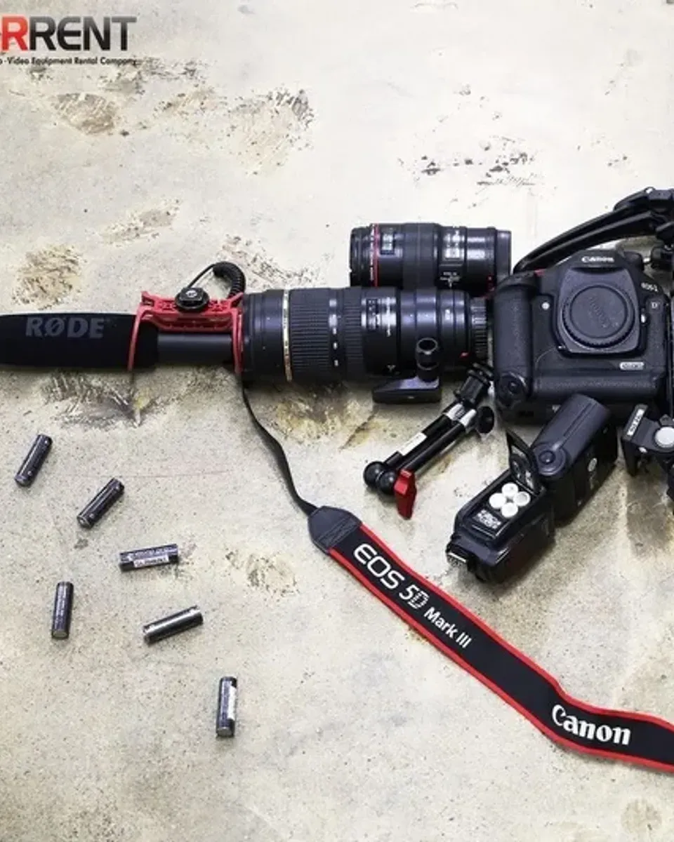 Rode shotgun microphone, telephoto zooms, and the gripped 5D Mark III body beside a speedlite loaded with AA batteries