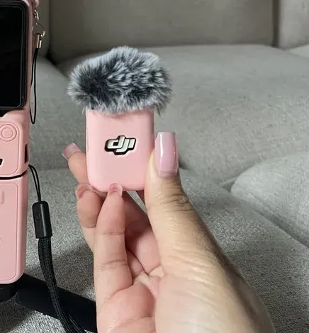 Close-up of the pink DJI Mic Mini transmitter with the fuzzy wind muff held in a hand