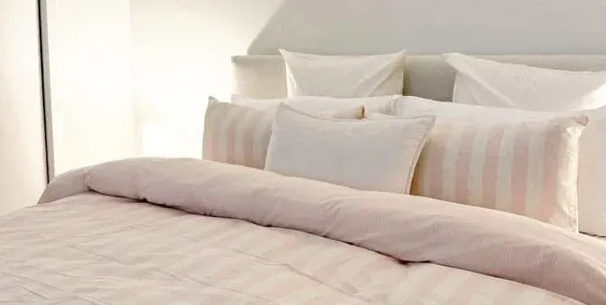 Pillowcases in striped pink pattern stacked on top of the gingham duvet