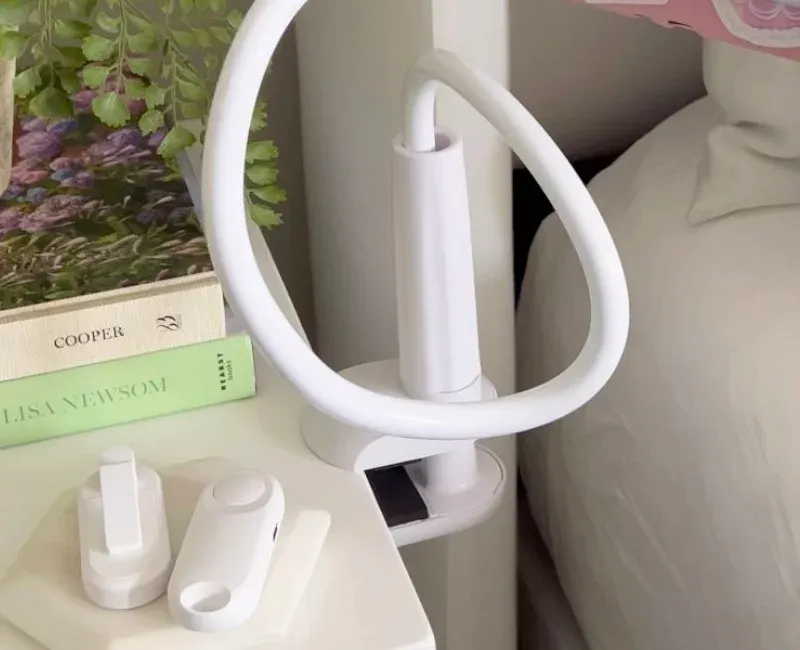 Clamped base of a gooseneck tablet holder on a white bedside table, arm bent overhead