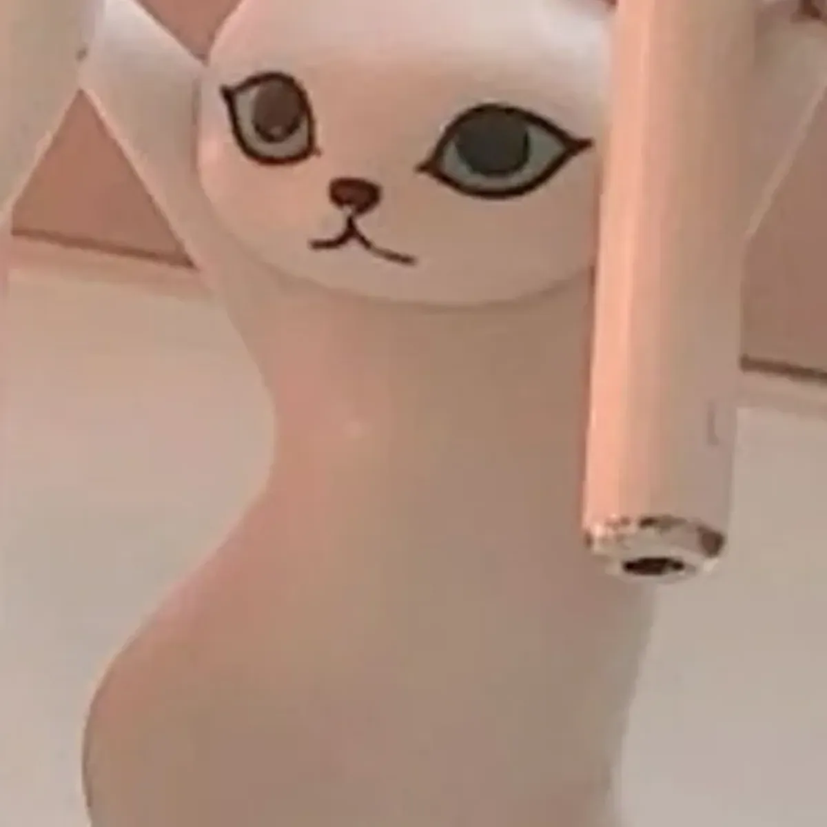 Close-up of the white cat figurine’s face holding a single AirPod in one raised paw