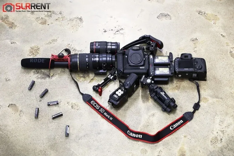 Canon 5D Mark III video rig with Rode microphone, telephoto lenses, speedlite, and AA batteries on a concrete floor