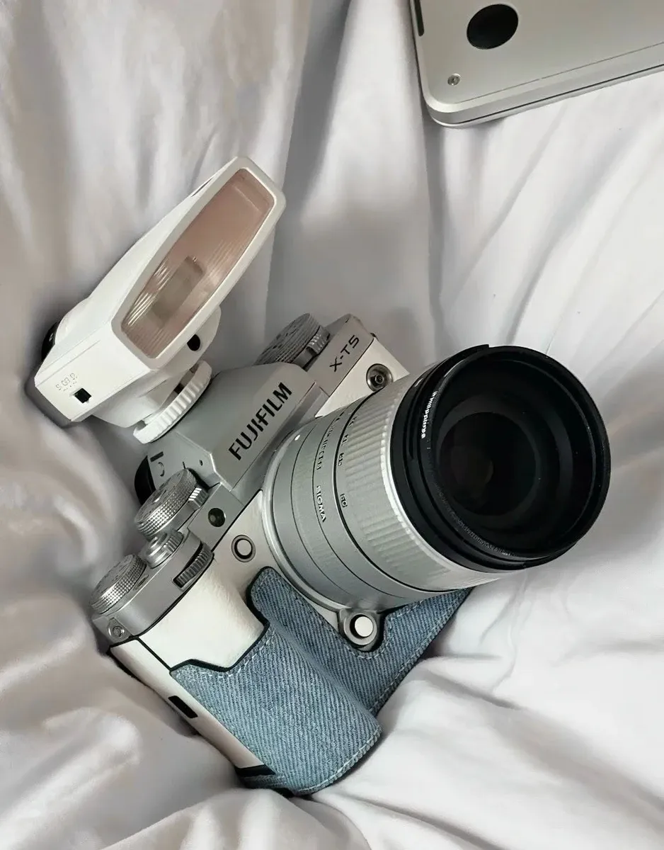Fujifilm X-T5 silver mirrorless camera with Sigma 18-50mm f/2.8 lens and white flash on white bedding