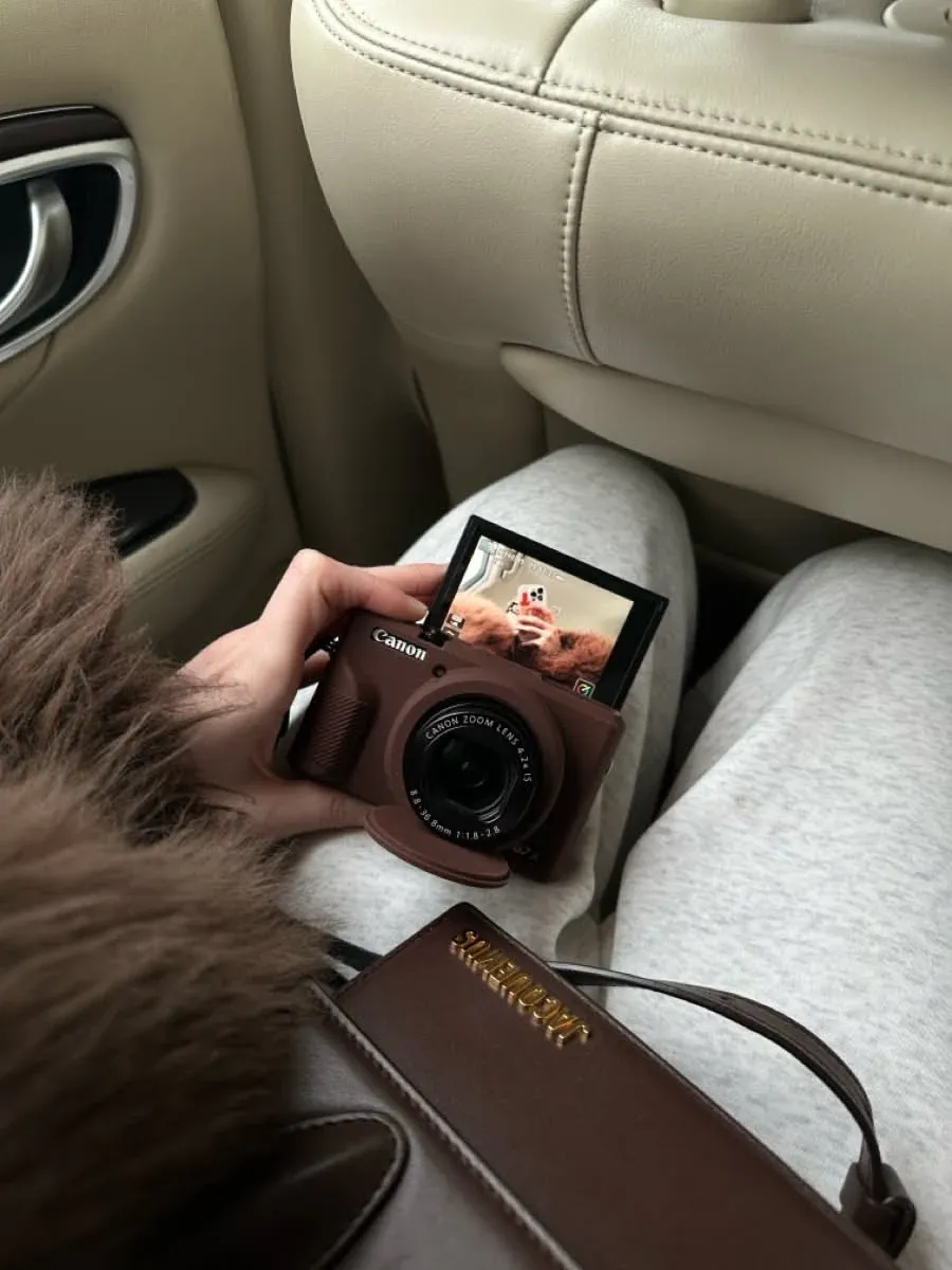 Canon G7 X Mark III held in hand showing flip-up screen and brown leather case