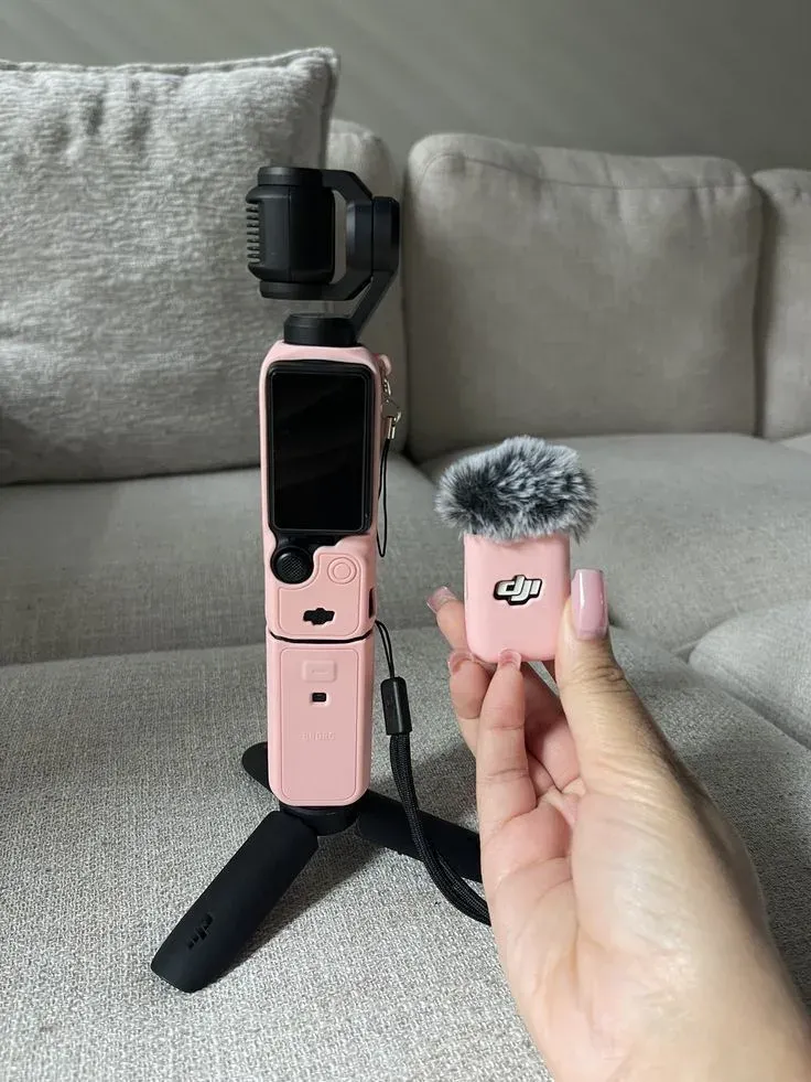 DJI Osmo Pocket 3 in a pink silicone case standing on its mini tripod next to the pink Mic Mini transmitter