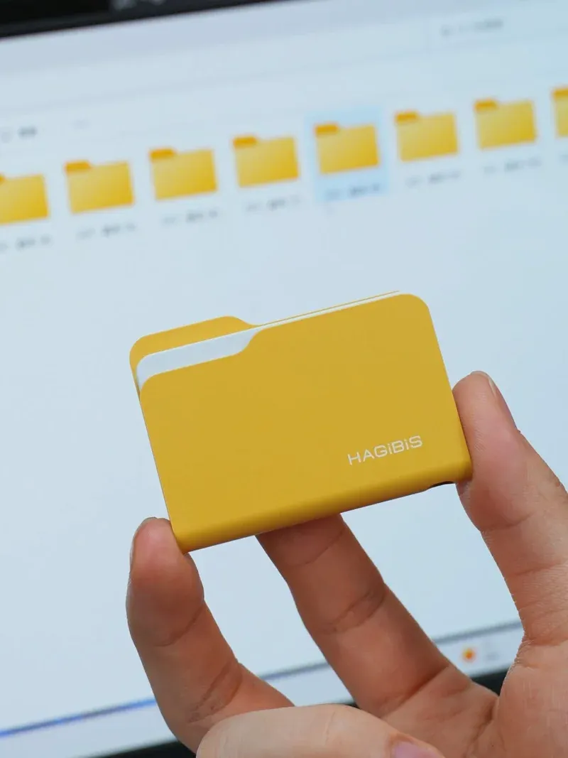 Yellow Hagibis folder-style NVMe enclosure with the white paper corner sticking out of the top